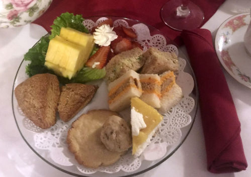 A plate of assorted snacks including sandwiches, cookies, fruit, and scones, garnished with lettuce and cream.