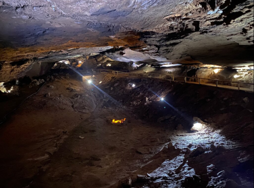 Dimly lit cave interior with rocky ground and beams of light illuminating the walls and pathways.