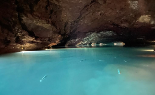 A serene underground cave with turquoise water and soft lighting reflecting off the rocky walls.