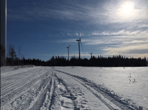 A snowy landscape with wind turbines in the background under a clear blue sky and bright sun.