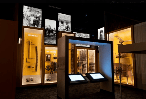 Museum exhibit featuring illuminated display cases with historical artifacts and photographs on the walls.