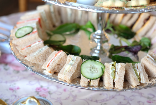 A tiered platter of assorted sandwiches, including cucumber and cream cheese, arranged with fresh greens.