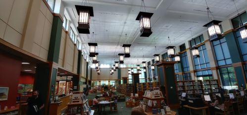 A spacious library interior with tall windows, wooden bookshelves, and decorative hanging lights.