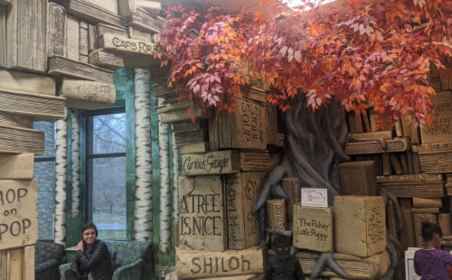 A cozy reading nook with book-themed decor, featuring a tree and autumn leaves, inviting relaxation and imagination.