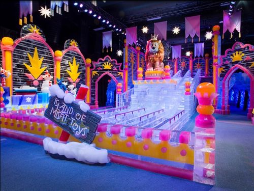 Colorful ice sculpture display featuring a lion, with a sign reading "Island of Misfit Toys" and vibrant decorations.