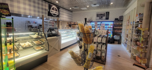 A bright deli interior featuring a display case, shelves of snacks, and a popcorn stand in the foreground.