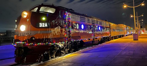 A brightly lit train decorated with colorful lights, parked on a platform at night.