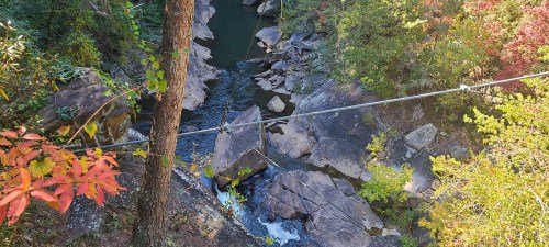 A serene river flows through rocky terrain, surrounded by vibrant autumn foliage and tall trees.