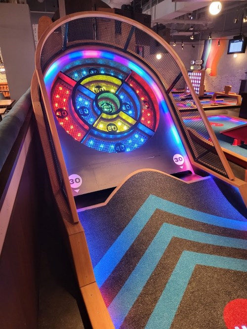 A colorful arcade game with a sloped ramp and illuminated target board, set in a vibrant gaming environment.
