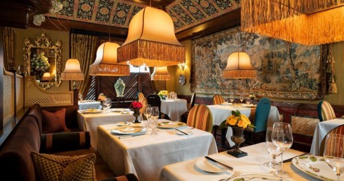 Elegant restaurant interior with ornate decor, soft lighting, and beautifully set tables featuring floral centerpieces.