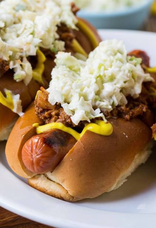 Two hot dogs topped with chili, mustard, and a generous serving of coleslaw on a white plate.