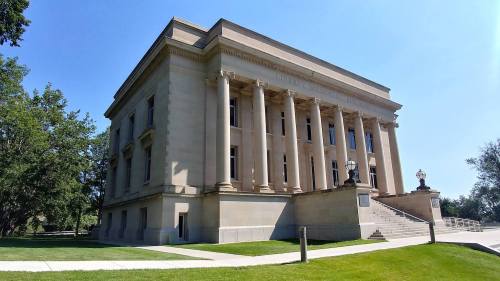 A grand building with classical architecture, featuring tall columns and a landscaped lawn under a clear blue sky.