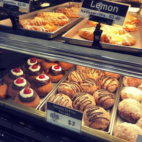 A display case filled with various pastries, including paczki topped with cream and cherries, and lemon pastries.