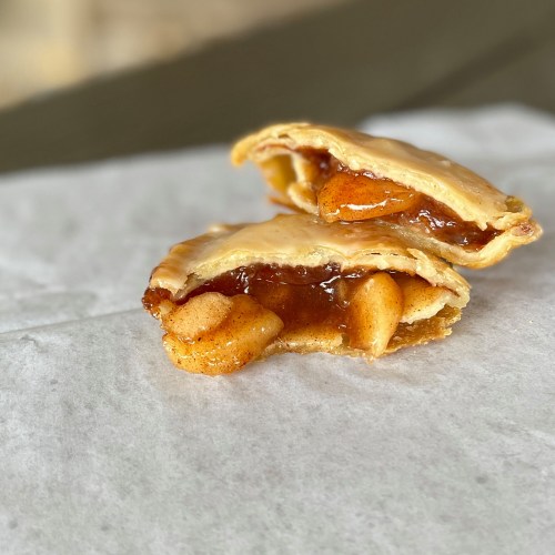 Two apple-filled pastries on a piece of parchment paper, showcasing a golden-brown crust and gooey filling.