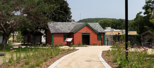 A red building with green trim surrounded by a garden and pathway, set in a sunny outdoor park.