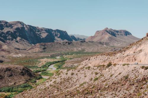 A scenic view of mountains and a winding river in a desert landscape under a clear blue sky.