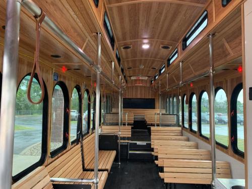 Interior of a wooden-paneled trolley with empty wooden benches and overhead grab bars, illuminated by soft lighting.