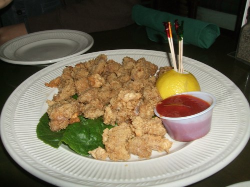 A plate of fried seafood, garnished with lettuce, a lemon wedge, and a small cup of dipping sauce.