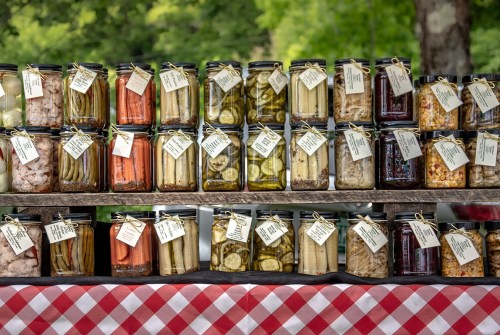 A display of various jars filled with colorful pickled vegetables and fruits, labeled and arranged on a table.