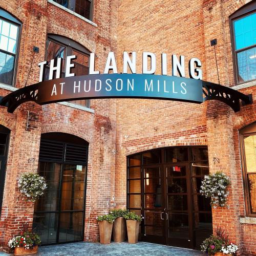 Sign for "The Landing at Hudson Mills" above a brick archway, with potted plants on either side.