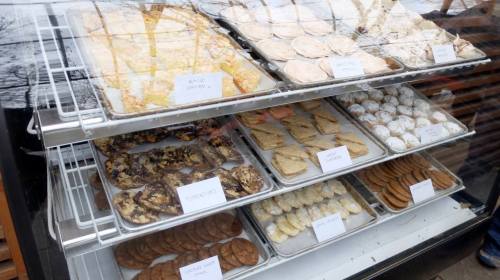 A display case filled with various baked goods, including cookies, bars, and pastries, all labeled with names.