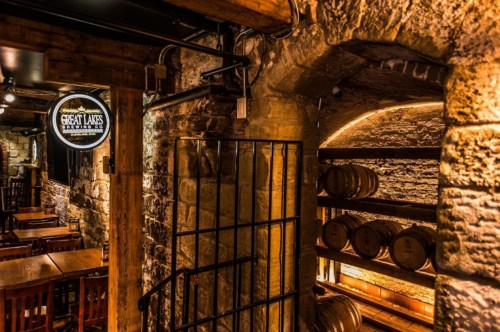 A cozy restaurant interior featuring stone walls, wooden tables, and a display of barrels in a dimly lit setting.