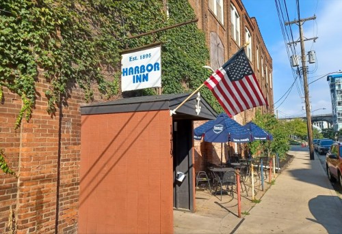 Exterior of Harbor Inn, established 1895, featuring an American flag and outdoor seating along a brick wall.