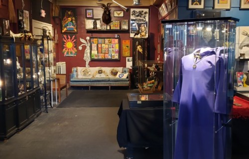 A colorful art gallery featuring display cases, a purple garment, and various artworks on the walls.