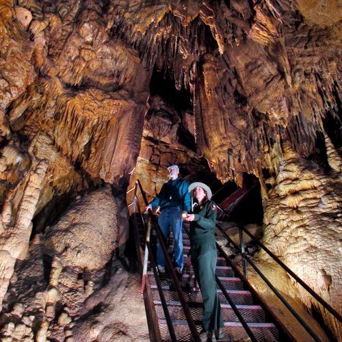 Two people on a staircase in a cave, surrounded by impressive stalactites and rock formations.