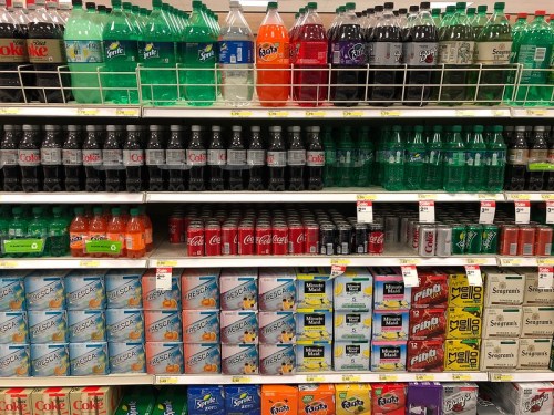 A grocery store shelf filled with various soda bottles and cans in different colors and brands.