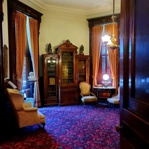 A vintage room with ornate furniture, a glass cabinet, and rich curtains, featuring a patterned carpet and warm lighting.