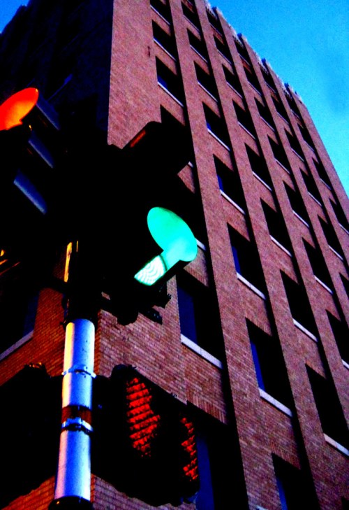 Traffic light showing green against a backdrop of a tall brick building at dusk.