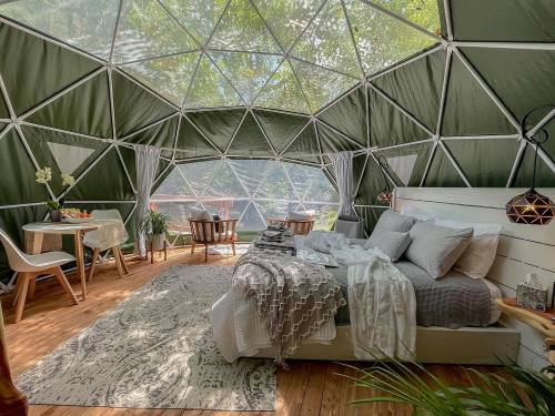 Cozy interior of a geodesic dome with a bed, dining area, and large windows letting in natural light.