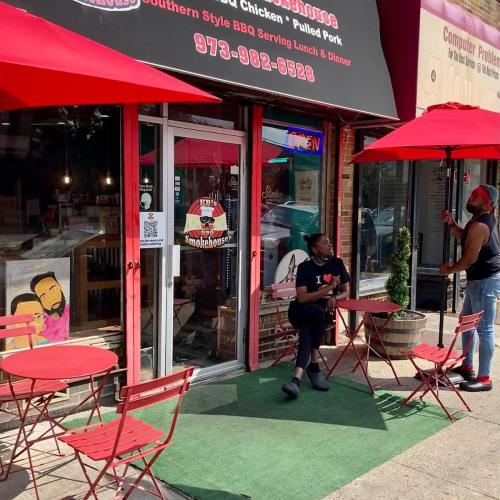A small BBQ restaurant with red outdoor seating and umbrellas, featuring a sign for lunch and dinner services.