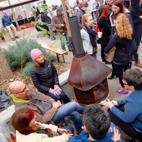 A group of people gathered around a fireplace in a cozy outdoor setting, chatting and enjoying each other's company.