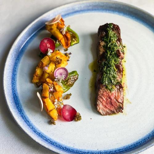 A plate featuring grilled steak with herb sauce, accompanied by a colorful salad of vegetables and fruits.