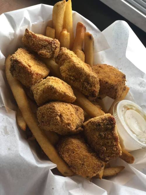 A basket of golden-brown fried nuggets and crispy French fries, served with a small cup of dipping sauce.
