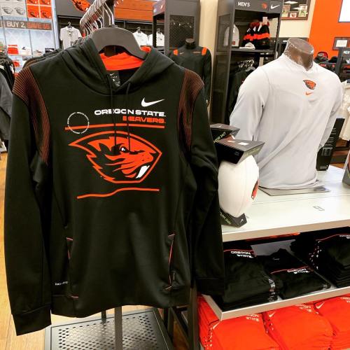 Black Nike hoodie with Oregon State Beavers logo displayed in a sports store, surrounded by other apparel.
