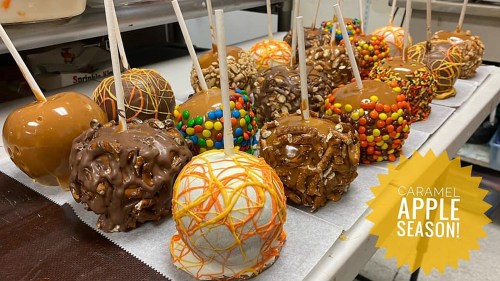 A variety of decorated caramel apples on a tray, featuring toppings like chocolate, nuts, and candy, with a "Caramel Apple Season!" graphic.