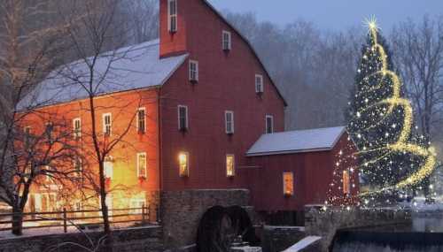 A red barn illuminated at night, with a sparkling Christmas tree beside it and snow-covered surroundings.