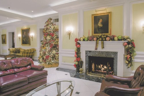 Cozy lobby with a decorated Christmas tree, elegant furniture, and a fireplace adorned with festive decorations.