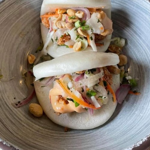 Two bao buns filled with shredded vegetables, peanuts, and a creamy sauce, served on a gray plate.