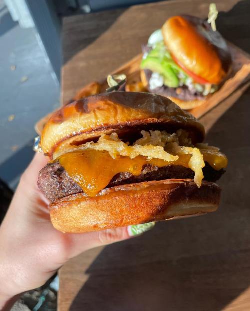 A hand holding a juicy burger with melted cheese and crispy onions, set against a wooden table.
