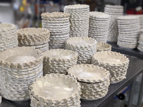 A large stack of unbaked pie crusts in various sizes, arranged neatly on a table in a kitchen setting.