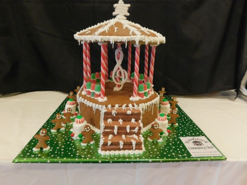 A festive gingerbread gazebo decorated with candy canes, icing, and gingerbread figures on a green polka dot base.