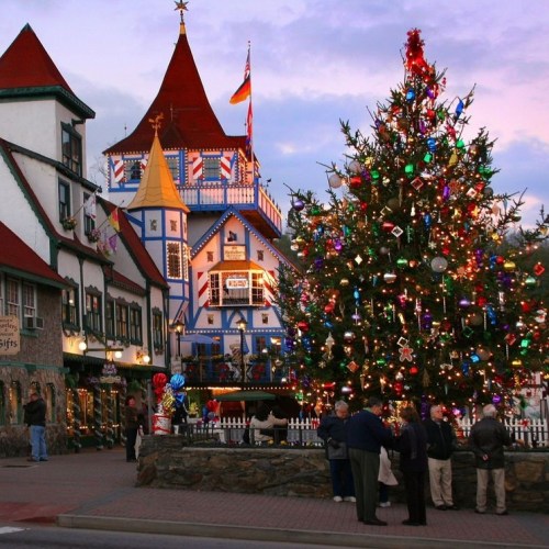 A festive town square with a decorated Christmas tree and charming buildings, illuminated at dusk.