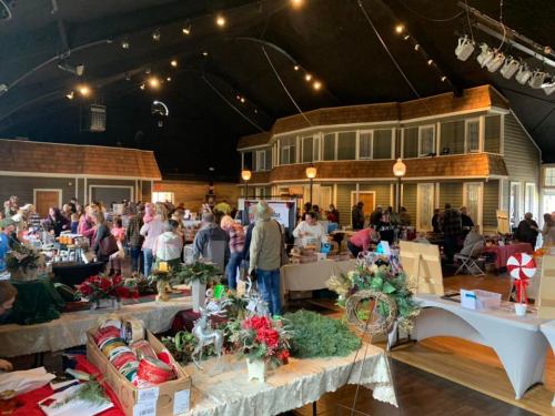 A bustling indoor market with vendors and shoppers, featuring holiday decorations and crafts in a festive atmosphere.