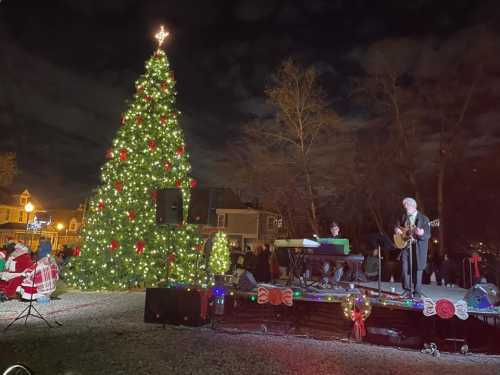 A festive scene with a large decorated Christmas tree and musicians performing on stage at night.