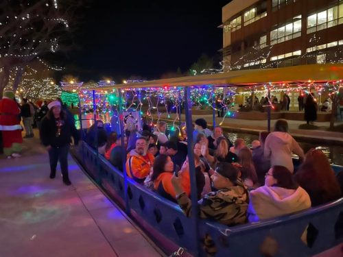A festive boat filled with people, surrounded by colorful lights and decorations at night.