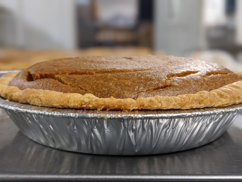 A freshly baked pumpkin pie in a silver pie tin, with a golden-brown crust and a smooth, spiced filling.